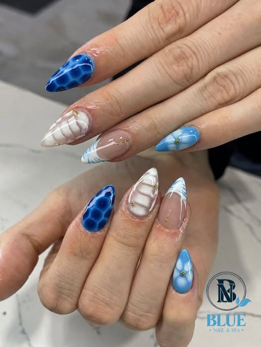 Blue and white patterned nail art with gold accents by Blue Nails & Spa, Tallahassee, FL